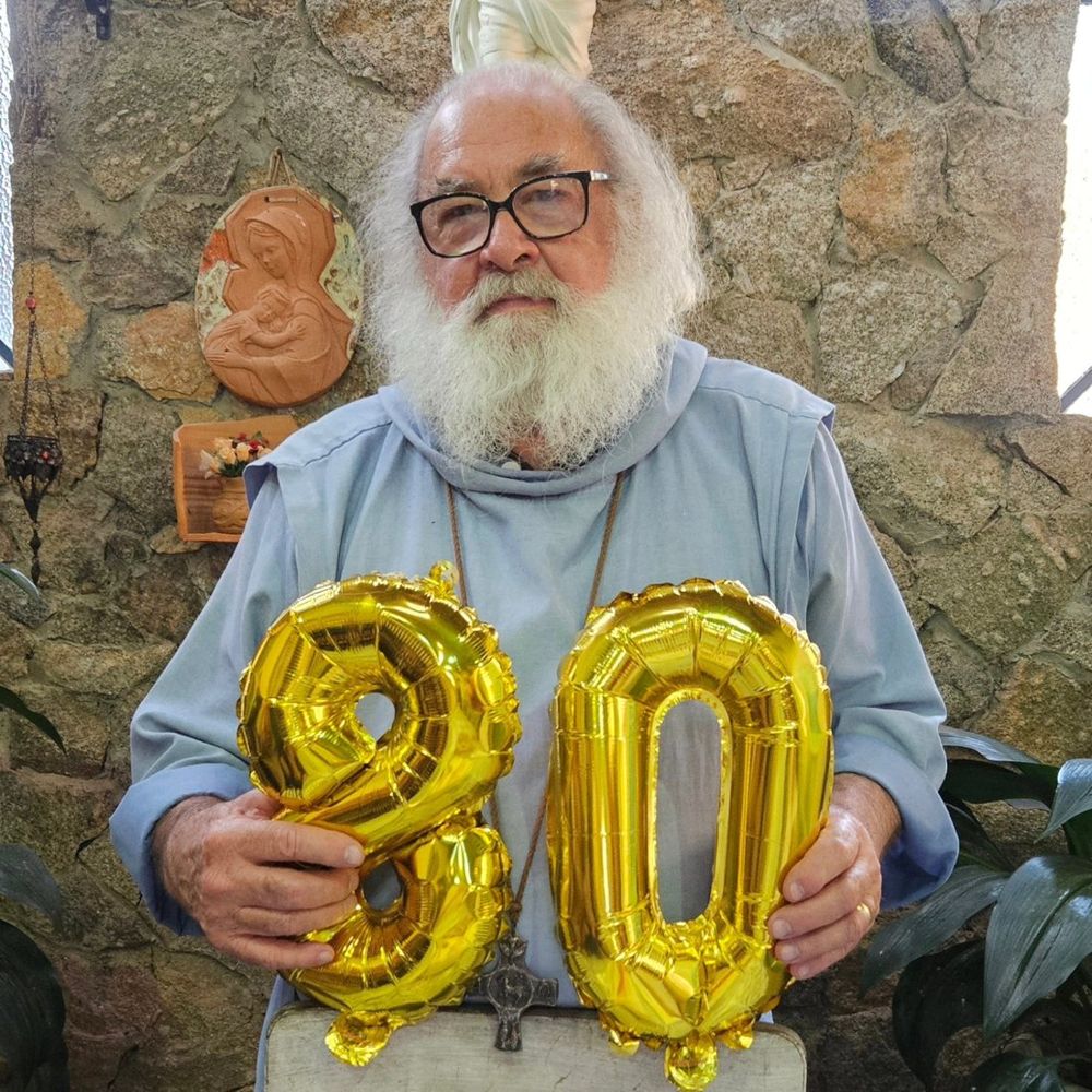 Irmão Bernardo da Esperança segurando balões dourados com o número 80, celebrando seu aniversário